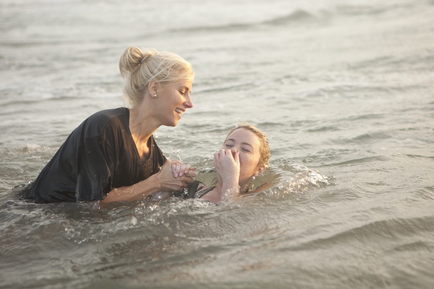une femme baptise une autre femme par immersion dans l'océan