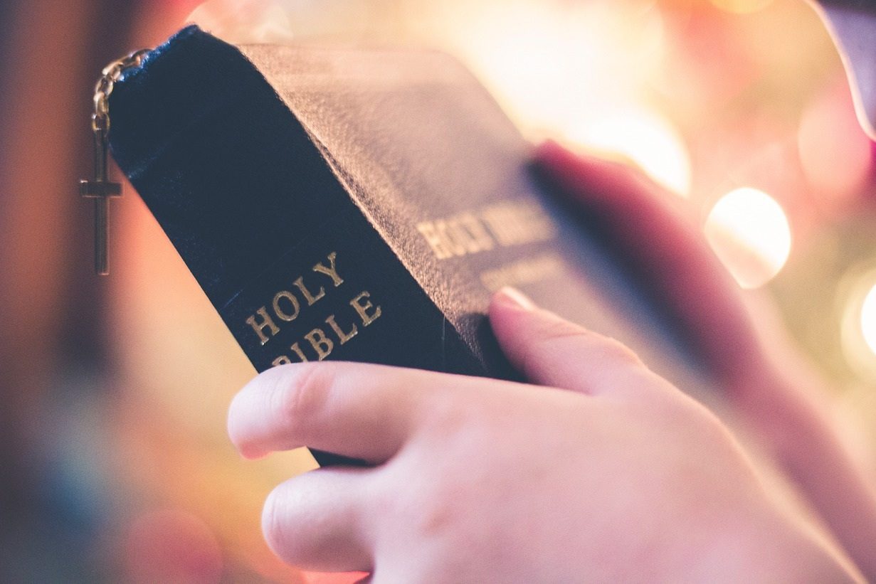 Des mains tiennent une une bible avec l'inscription "Holy Bible"