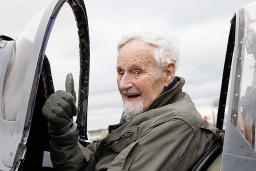 Jack Hemmings, cheveux et barbe grisonnants, le pouce en l'air à l'intérieur d'un cockpit d'un avion de la MAF