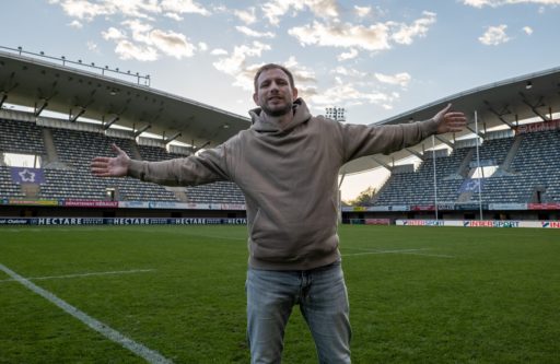 L'aumônier Joël Thibault les bras tendus au milieu de la pelouse d'un terrain de rugby