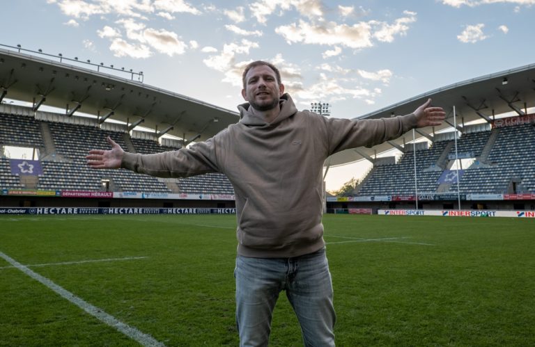 L'aumônier Joël Thibault les bras tendus au milieu de la pelouse d'un terrain de rugby