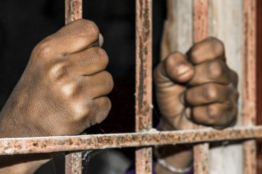 Des mains brunes tiennent les barreaux d'une prison