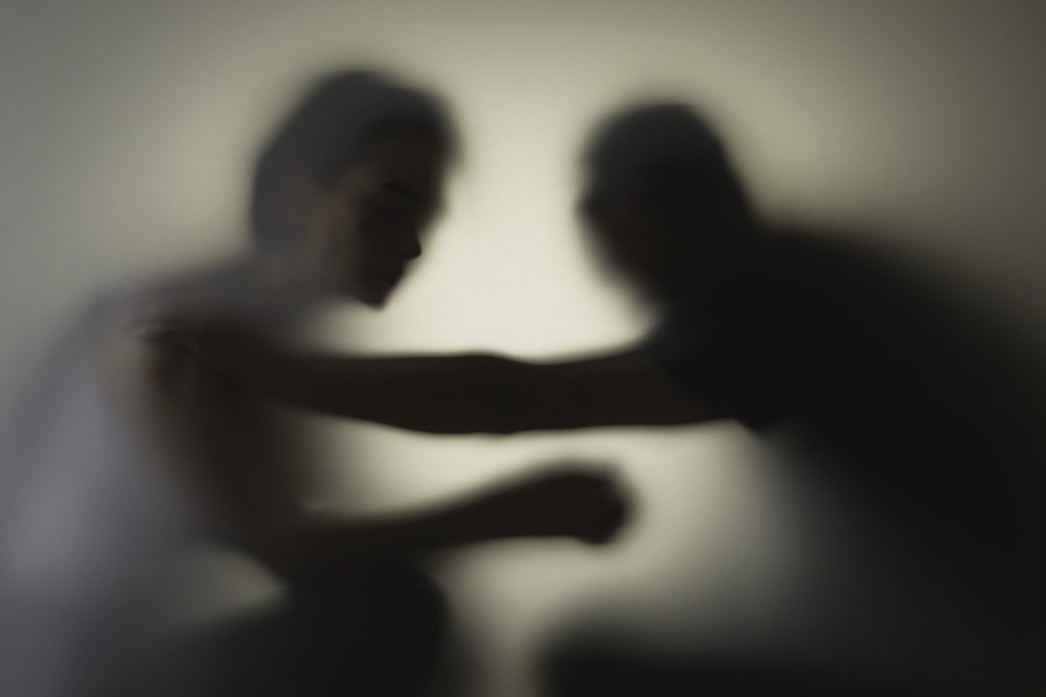 Un homme met la main sur l'épaule d'une femme derrière une vitre laissant simplement apparaître les silhouettes