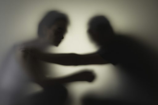 Un homme met la main sur l'épaule d'une femme derrière une vitre laissant simplement apparaître les silhouettes