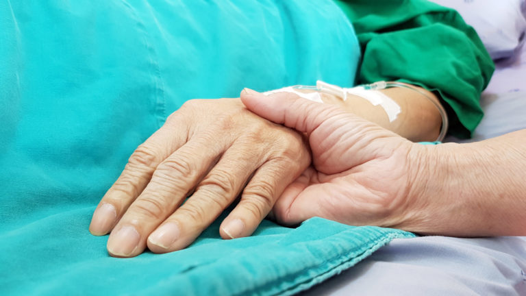 La main d'un patient est couverte par la main d'un soignant, dans un milieu hospitalier