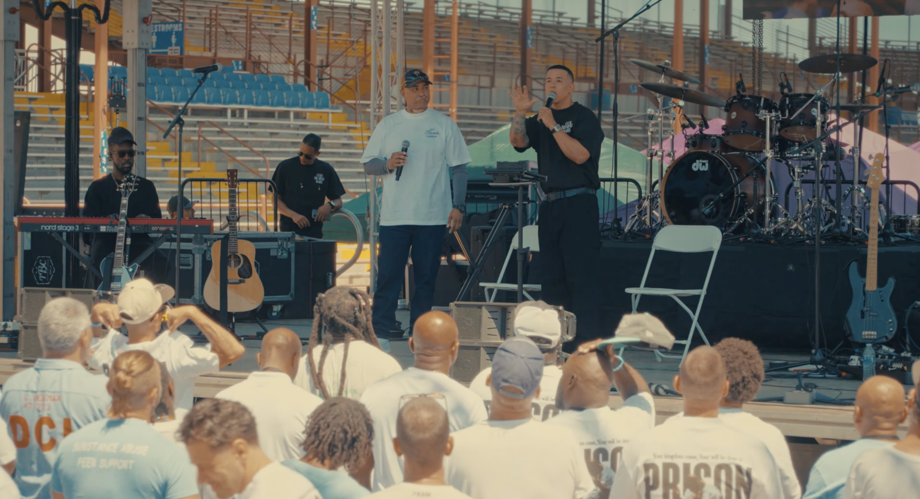 Traduit par un pasteur, Daddy Yankee se tient debout sur une scène et prêche devant des détenus également debout, de dos.